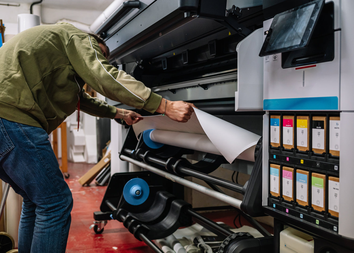 Person operating a large printing machine with paper in a print shop.

